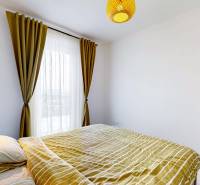 Ložnice v třípokojovém bytě s postelí, policemi a závěsy.