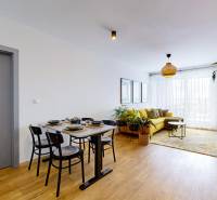 Obývací pokoj v 3-pokojovém bytě s podlahou s dřevěným dekorem, žlutou sedačkou a jídelním stolem.