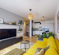 Obývací pokoj se žlutou sedačkou, nástěnnými dekoracemi a podlahou s dřevěným dekorem v 3-pokojovém bytě.