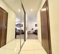 Chodba v 2-pokojovém bytě s dlažbou, zrcadlem a výhledem do obývacího pokoje.