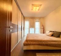 Ložnice v 2pokojovém bytě s velkou postelí a podlahou s dřevěným dekorem.