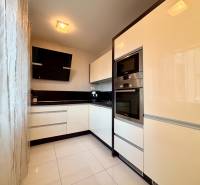 Bílá kuchyně s černými akcenty a spotřebiči v 2pokojovém bytě.