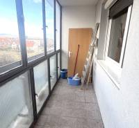 Zasklený balkon 3pokojového bytu s dlažbou, výhledem na okolí a uskladněným nářadím.