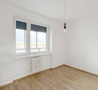 Pokoj v 3-pokojovém bytě s podlahou s dřevěným dekorem a bílými stěnami.