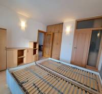 Ložnice ve 4pokojovém bytě s nábytkem v dřevěném dekoru a postelí bez matrace.