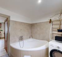 Koupelna v rodinném domě s rohovou vanou, pračkou a květinami.