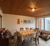 Jídelna v rodinném domě s dřevěným stropem, čtvercový stůl, velké okno.