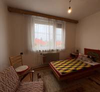 Pokoj s postelí, křeslem a dekorativním kobercem na stěně v rodinném domě.