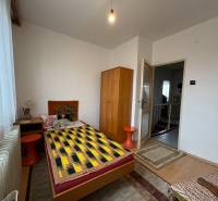 Pokoj v rodinném domě s jednolůžkem, skříňkou a podlahou s dřevěným dekorem.