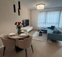 Obývací pokoj v dvoupokojovém bytě s šedou sedačkou, jídelním stolem a podlahou s dřevěným dekorem.