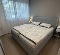 Ložnice v 2-pokojovém bytě s postelí, nočními stolky a podlahou s dřevěným dekorem.