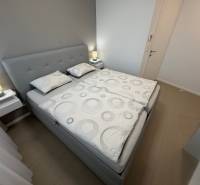 Ložnice s manželskou postelí a podlahou s dřevěným dekorem v dvoupokojovém bytě.