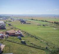 Pozemky - bydlení v Mlynici; rozestavěné domy a rozsáhlá pole pod slunečnou oblohou.