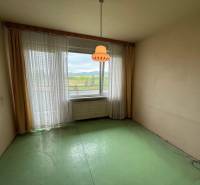 Pokoj se zelenou podlahou a velkým oknem ve 3-pokojovém bytě.