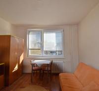 Garsonka s pohovkou, stolem a skříní, podlaha s dřevěným dekorem.