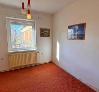 Pokoj v rodinném domě, podlaha pokrytá kobercem, bílý radiátor, obrazy na stěnách.