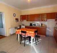 Kuchyně v rodinném domě s dřevěným dekorem a oranžovým ubrusem na stole.