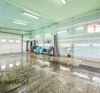 Místnost v budově s mokrou dlažbou, umyvadlem a hadicí na stěně.