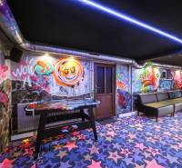 Interiér budovy s graffiti na stěnách, barevné koberce a stolní hokej.