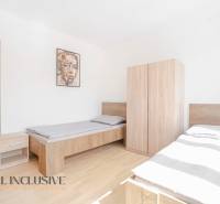 Ložnice s dvěma postelemi a nábytkem, podlaha s dřevěným dekorem, obraz na stěně.