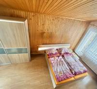 Ložnice v rodinném domě s dřevěným obkladem, podlaha s dřevěným dekorem, velké okno.