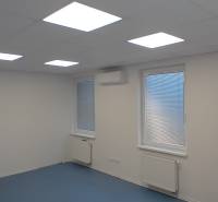 Kanceláře s bílým stropem, modrou podlahou a okny se žaluziemi.