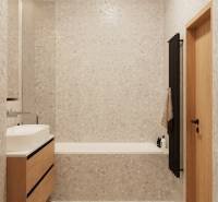 Koupelna se světlým obkladem, dřevěnou skříňkou pod umyvadlem a tmavým žebříkovým radiátorem.