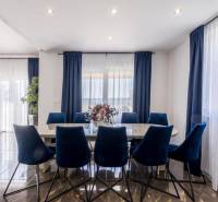 Jídelna ve vile s tmavými závěsy, podlahou s dřevěným dekorem a modrými židlemi.