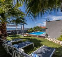 Útulná zahrada s bazénem ve vile v Kaštelu, obklopená palmami a lehátky.