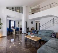 Obývací pokoj vily s pohodlnou sedačkou, jídelnou a schodištěm, podlaha s dřevěným dekorem.