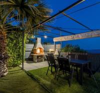 Palmová zahrada vily v Kaštela s pergolou, krbem a stolem.