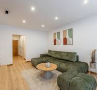 Obývací pokoj v 2-pokojovém bytě s podlahou s dřevěným dekorem, zelená sedačka, konferenční stolek.