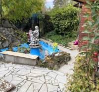 Zahrada chaty v košické městské části Vyšné Opátske s cihlovým domkem a sochou.