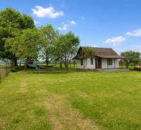 Chata v Obeckově obklopená přírodou s udržovaným trávníkem a dřevinami.