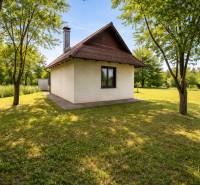 Chata v Obeckově obklopená zeleným trávníkem a stromy.