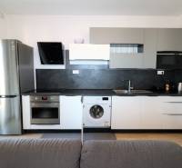 Kuchyně v 2-pokojovém bytě se šedými skříňkami, spotřebiči a podlahou s dřevěným dekorem.