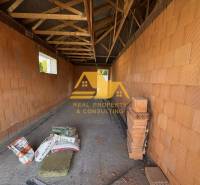 Stavba rodinného domu na ulici v Nových Zámcích s cihlovými stěnami a trámovým stropem.