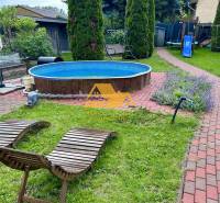 Zahrada chaty v Nových Zámcích s bazénem, lehátky a dětským hřištěm.