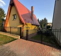 Chata na ulici v Nových Zámcích, se špičatou střechou a cihlovým komínem.