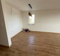 Pokoj dvoupokojového bytu s podlahou s dřevěným dekorem a závěsnými svítidly.