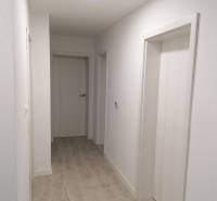 Úzká chodba v rodinném domě s bílými stěnami a podlahou s dřevěným dekorem.