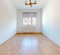 Prázdná místnost s podlahou s dřevěným dekorem v 3-pokojovém bytě, jednoduché stěny a okno.