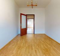 Pokoj v 3-pokojovém bytě s podlahou s dřevěným dekorem a bílými stěnami.