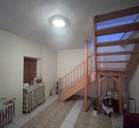 Interiér rodinného domu s dřevěným schodištěm, stolkem a podlahou z keramických dlaždic.