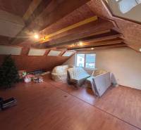 Podkrovní pokoj v rodinném domě s podlahou s dřevěným dekorem a střešními okny.