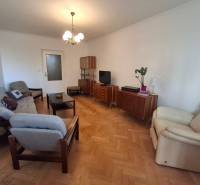 Obývací pokoj třípokojového bytu s podlahou s dřevěným dekorem, retro nábytkem a pohodlnými křesly.