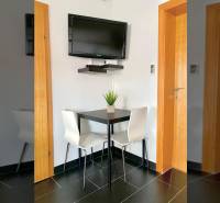 Jídelna v rodinném domě s rohovým stolem, televizorem na stěně a černými dlaždicemi.