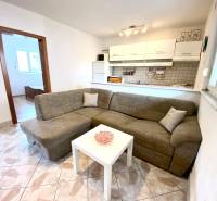 Interiér rodinného domu s pohovkou, bílým stolem a kuchyňským koutem.