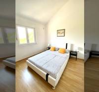 Ložnice v rodinném domě s podlahou s dřevěným dekorem, postelí a oknem.