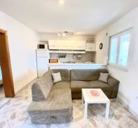 Obývací pokoj v rodinném domě s pohovkou a kuchyňským koutem, dlažba na podlaze.